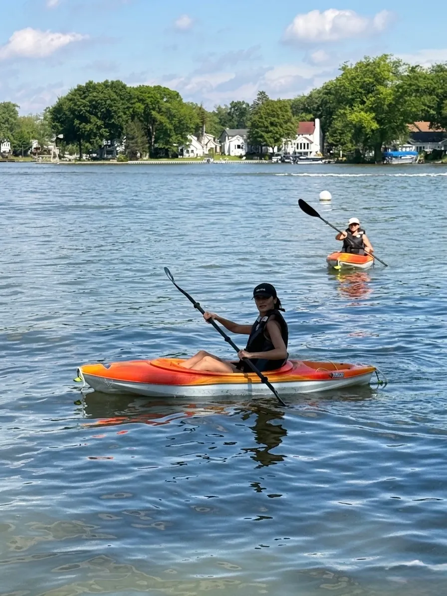 Two guests paddling orange kayaks on the lake on a sunny day, with lakefront homes across the water