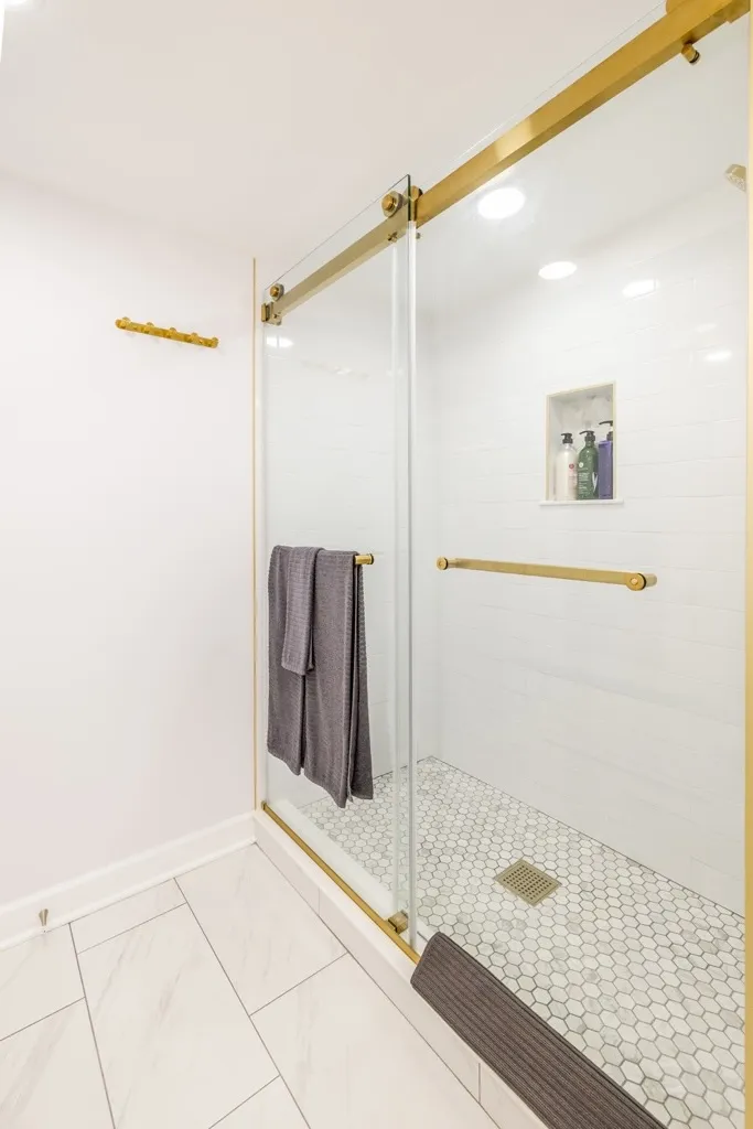 Walk-in tiled shower with gold fixtures and glass doors