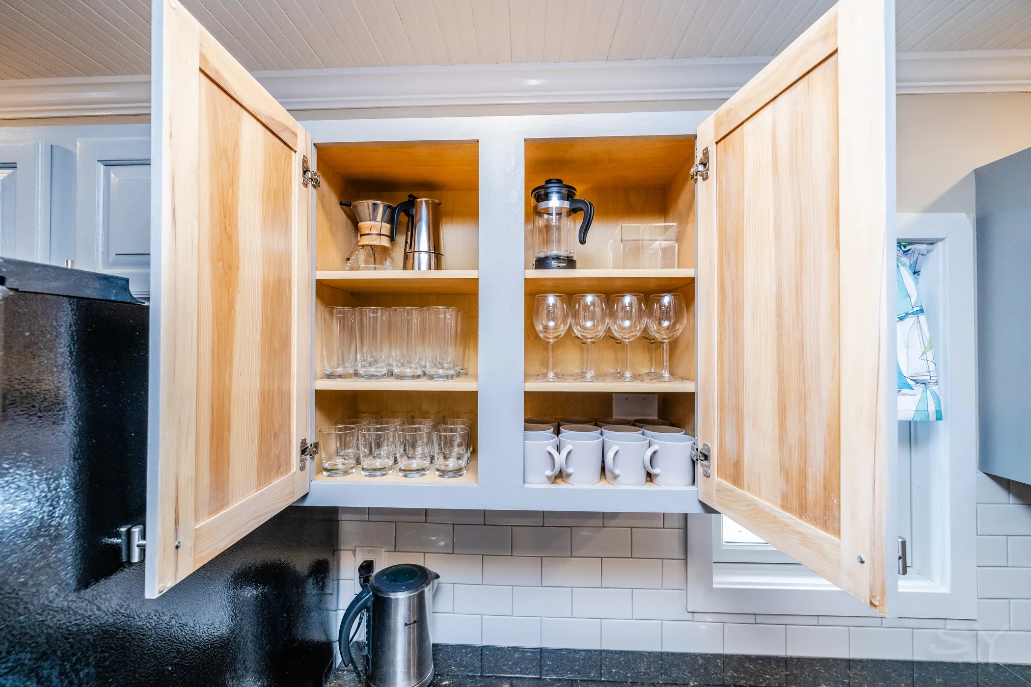 Open cabinets stocked with glassware, mugs and coffee makers