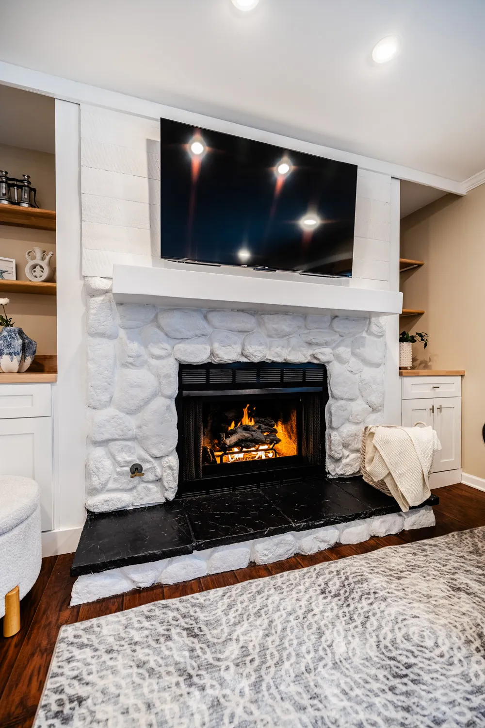 White stone fireplace with a mounted TV and built-in shelving